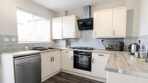 A modern kitchen with white cabinets, a dishwasher, a stove, an oven, a microwave, and a kettle. - 4 Plas Newydd (Llandudno)