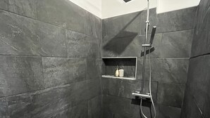 A small, dark-toned shower room with a handheld showerhead and a wall-mounted faucet. - Le studio du manoir (Puna'auia)