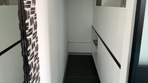 A narrow hallway with a black and white patterned curtain, a metal rod for hanging clothes, and a tiled floor. - Le studio du manoir (Puna'auia)