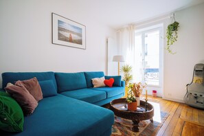 A living room with a blue sofa, a coffee table with a plant, a framed picture on the wall, and a view through a window. - Spacious & Quirky 1BD flat 10 mins to Sacré Coeur (Paris)