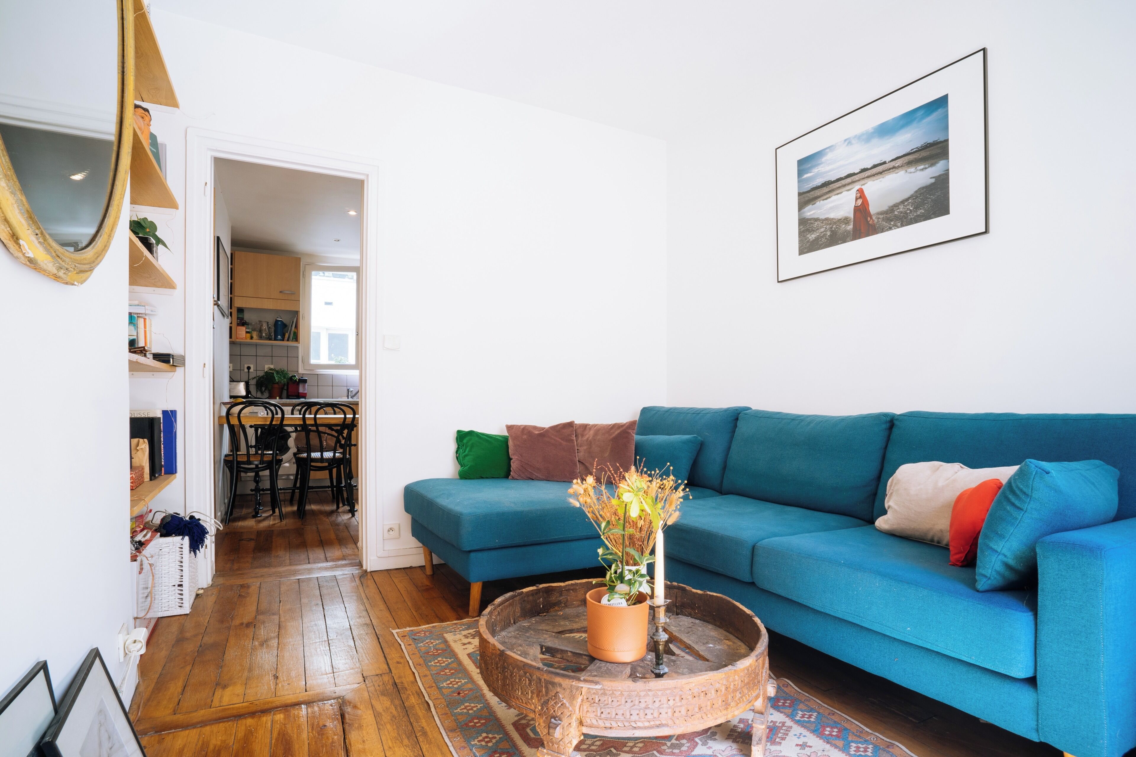 Un salon avec un canapé bleu, une table basse ornée d’une plante et un tableau encadré accroché au mur.