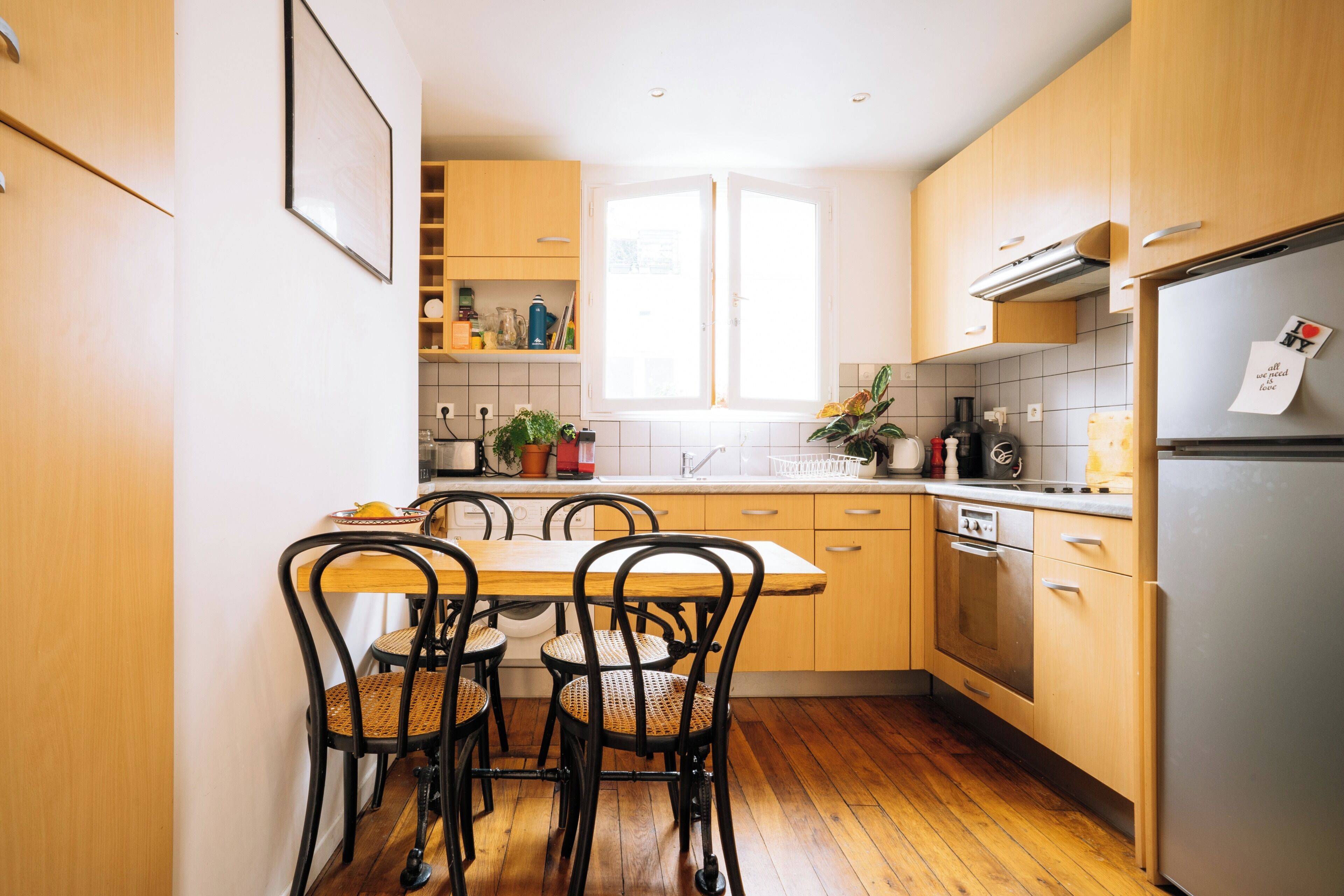 Une cuisine moderne avec des meubles en bois, un réfrigérateur en acier inoxydable et une table à manger avec quatre chaises.