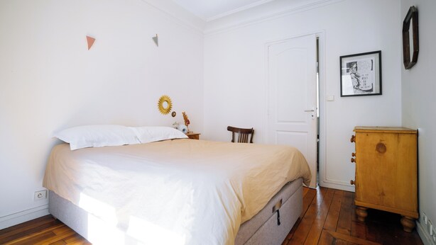 Een slaapkamer met een bed, een houten dressoir, een deur en een wand met een lijst eromheen.
