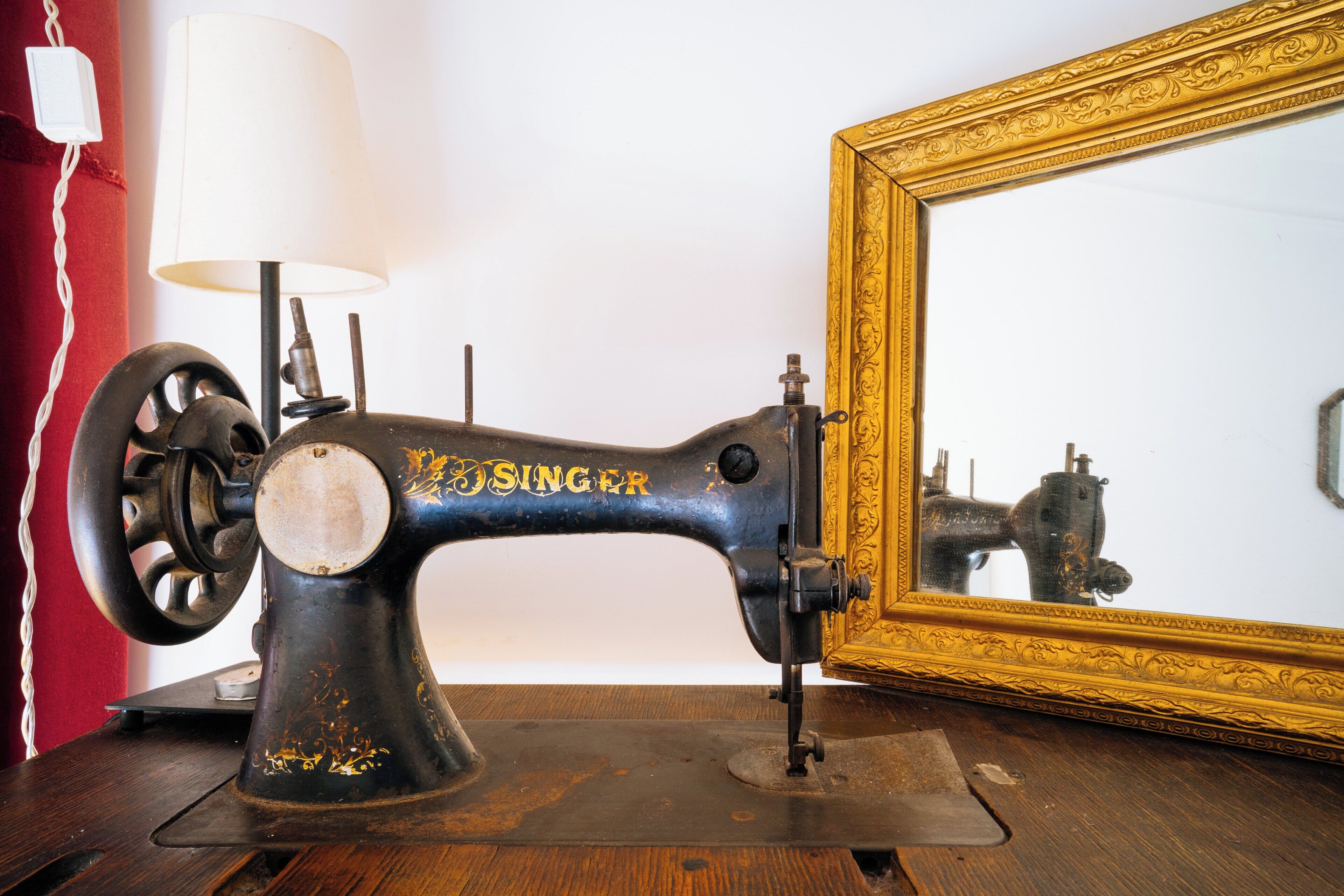 An antique Singer sewing machine on a wooden table with a red curtain and a framed mirror in the background.