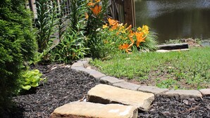 Un jardin avec un bassin, des pas japonais et des fleurs oranges.
