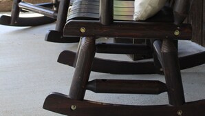 Deux fauteuils à bascule avec coussins, placés sur une terrasse en béton, avec une structure en bois en arrière-plan.