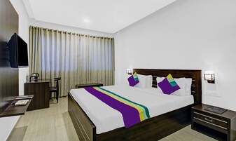 Habitación de hotel con cama, mesitas de noche, televisión y ventana con cortinas.