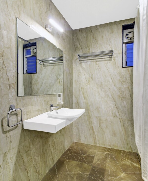 Un baño con pared de mármol, un lavamanos blanco, un espejo y una cortina de ducha.