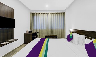 Habitación de hotel con cama, escritorio, silla, televisión y ventana con cortinas.