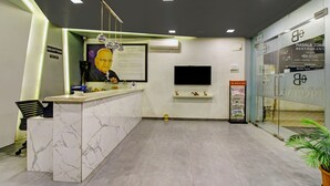 A reception area with a marble counter, a reception desk, a mounted television, and a glass wall with signage. - Treebo Premium Brijinn (Nagpur)