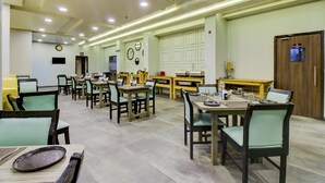 A spacious dining area with multiple tables and chairs, equipped with basic amenities like water bottles and cutlery. - Treebo Premium Brijinn (Nagpur)
