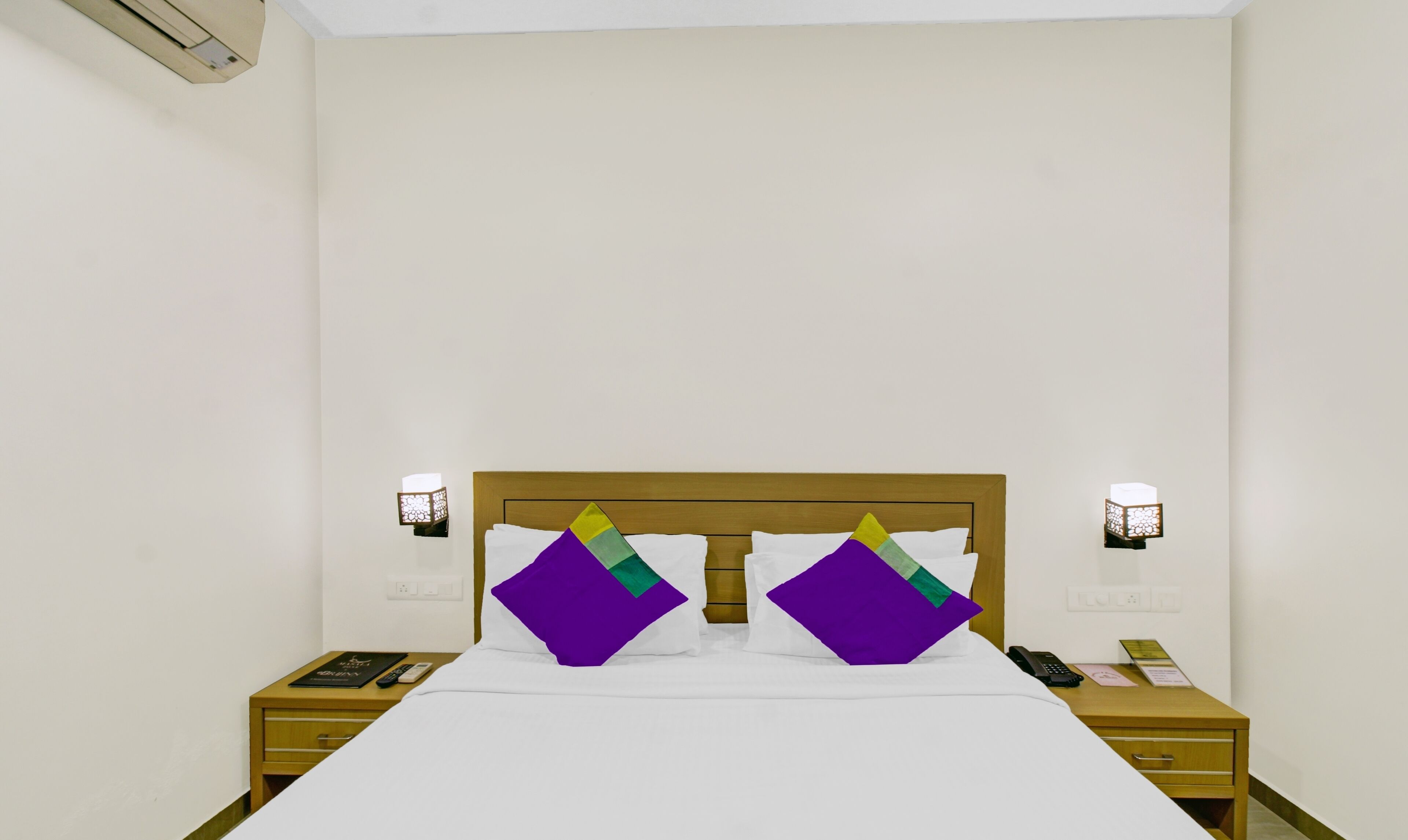 Ein Hotelzimmer mit hölzernem Kopfteil, weißer Bettwäsche und zwei Nachttischen mit Lampen und Telefon.
