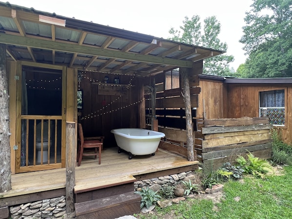A rustic cabin with a wooden porch, a bathtub, and a stone pathway leading to the entrance.