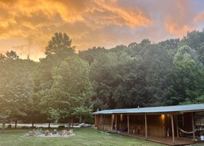 A rustic cabin with a porch, surrounded by a forested area.