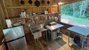 Uma cozinha rústica com paredes de madeira, uma geladeira de aço inoxidável e diversos utensílios de cozinha e panelas nas prateleiras.