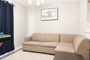 A beige sofa in a room with a white wall, a framed abstract artwork, and a blue curtain.