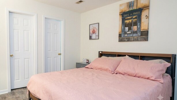 Un dormitorio con una cama, dos puertas, una mesita de noche y una pared con un cuadro.