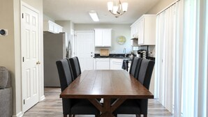 Un comedor con una mesa y sillas de madera, una cocina al fondo y un pasillo con puertas.
