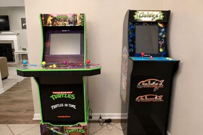 Due cabinati arcade, uno con Teenage Mutant Ninja Turtles e l'altro con Galaxian, in una stanza con camino e televisione.