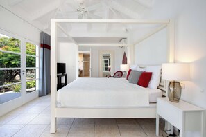 Un dormitorio con cama con dosel, una mesita de noche con lámpara, un televisor y vistas al exterior a través de un ventanal.