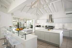 A modern kitchen with white cabinetry, a glass island with bar stools, and a large window providing natural light. - Encore (8 bedrooms) - Lovely villa with pool, Terres Basses, St. Martin (Terres Basses)
