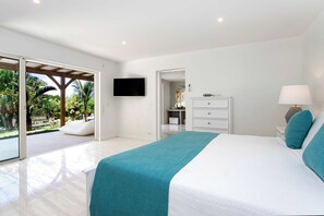 A modern bedroom with a large bed, a TV mounted on the wall, a dresser, and a view of a garden through a sliding door. - Encore (8 bedrooms) - Lovely villa with pool, Terres Basses, St. Martin (Terres Basses)