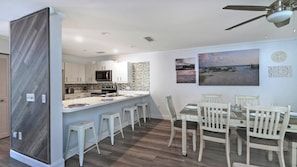 A modern kitchen with a central island, white bar stools, and a dining area with a table and chairs.