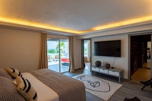 Habitación de hotel moderna con una cama grande, un televisor de pantalla plana, una puerta corrediza de vidrio hacia un balcón y una consola minimalista.