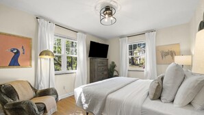 A bedroom with a bed, a chair, a TV, and windows with curtains. - Zan Court Unit 1 · Mt Lookout Hideaway (Cincinnati)