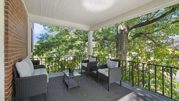 A covered balcony with wicker furniture and a glass table, overlooking a tree-lined street. - Zan Court Unit 1 · Mt Lookout Hideaway (Cincinnati)