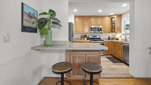 A modern kitchen with wooden cabinets, a stainless steel microwave, and a large island with stools. - Zan Court Unit 1 · Mt Lookout Hideaway (Cincinnati)