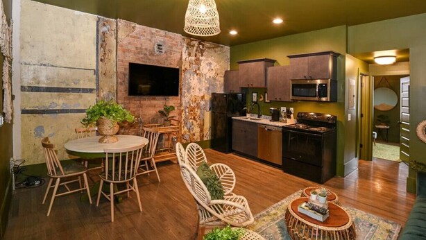 Una cocina compacta con electrodomésticos modernos, un comedor con sillas de mimbre y una pared de ladrillo rústico.