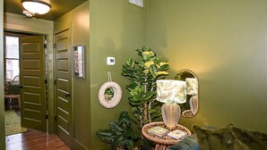 Un pasillo con pared verde, una mesita de mimbre, un sofá verde y una puerta que da a otra habitación.