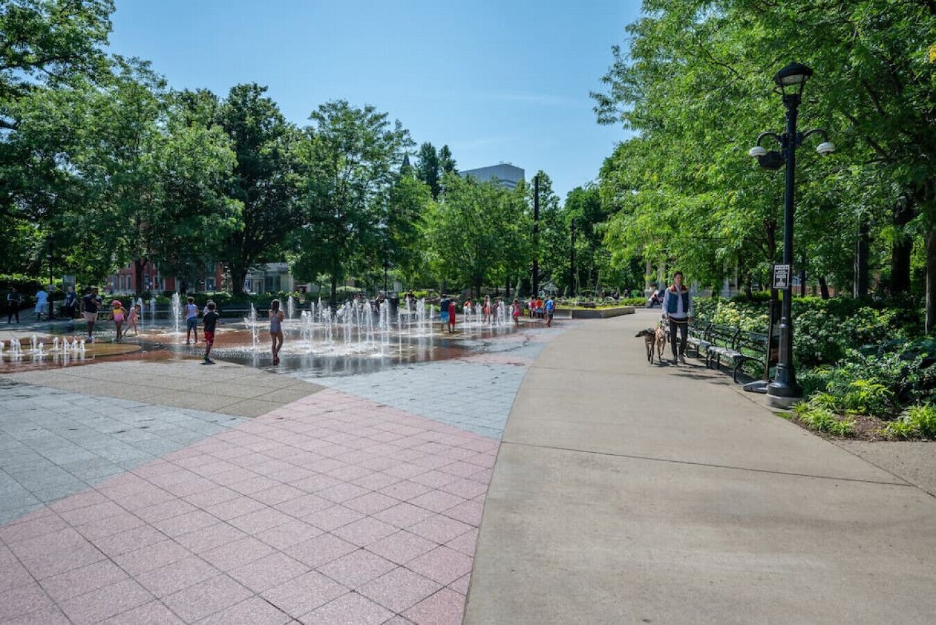 A public park with a water feature, paved walkways, and greenery.