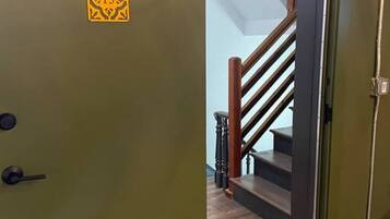 Una porta verde con un cartello giallo, una scala di legno e una parete di colore chiaro.