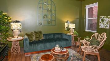 A cozy living room with a dark green sofa, wicker furniture, and decorative plants.