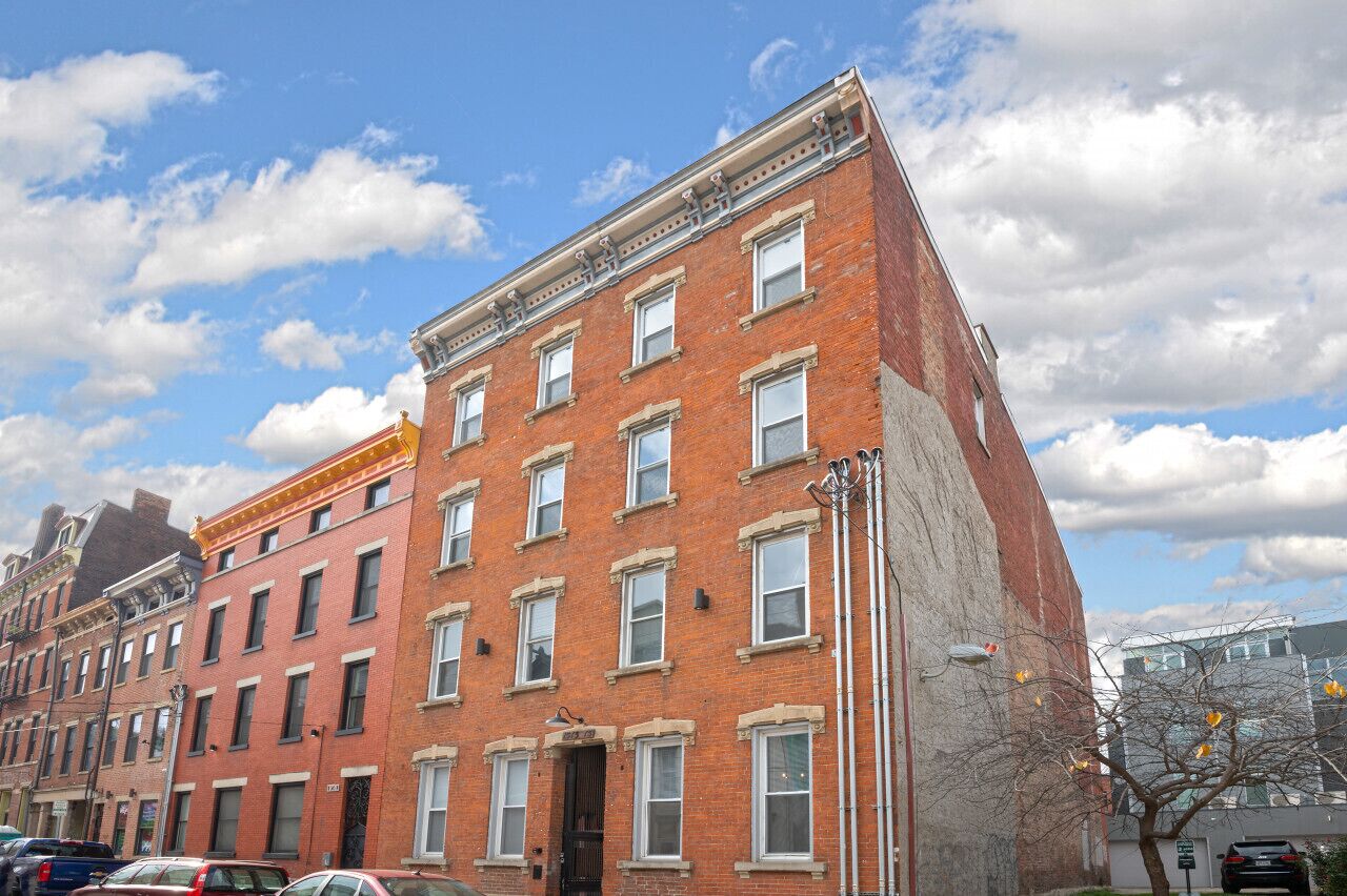 A multi-story brick building with a flat facade, multiple windows, and a corner entrance.
