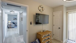 A hallway leading to a living area with a TV mounted on the wall, a wooden chest of drawers, and a welcome sign. - Indian Rocks Beach Unit B Star5vacations (Indian Rocks Beach)