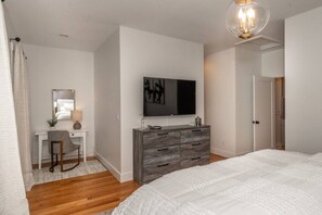 Quarto com uma cama grande, cômoda, escrivaninha com cadeira, televisão e porta.