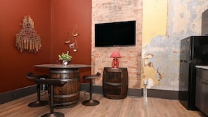 A room with a brick wall, a wooden barrel table with stools, a red lamp, and a flat-screen TV mounted on the wall. - Rodeo Red | OTR Cincinnati (Cincinnati)