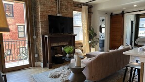 Een moderne woonkamer met een bakstenen muur, een open haard, een bank en een eethoek.