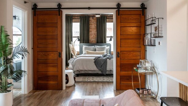 Een slaapkamer met een bed, bureau, stoel, een plant en een schuifdeur.
