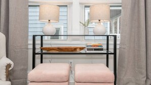 A room with a black metal console table, two white lamps, a wooden bowl, and two pink cushioned stools. - Lower Cambridge · Cozy Cambridge (Cincinnati)
