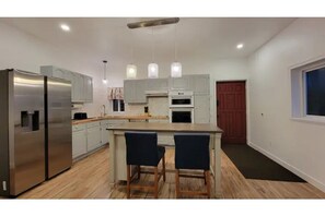 Una cocina moderna con electrodomésticos de acero inoxidable, una isla central con taburetes de bar e iluminación colgante.