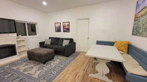 Una sala de estar con sofá, reposapiés, televisión, chimenea y una mesa de comedor.