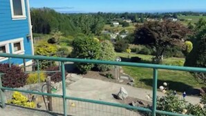 Un barrio residencial con una casa azul, una cerca verde y una vista despejada de un paisaje montañoso con árboles y casas.