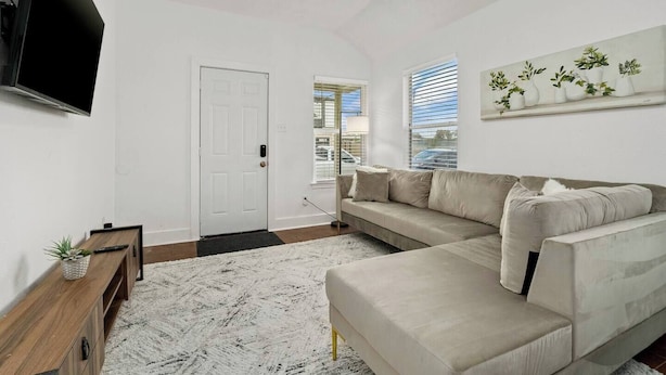 A modern living room with a beige sofa, a flat-screen TV, a wooden side table, and a white door. - Central Houston - Bright and Spacious Modern Mid - 4 miles to DT (Houston)