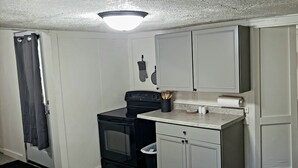 A compact kitchen with white cabinets, a black stove, and a countertop with a roll of paper towels.