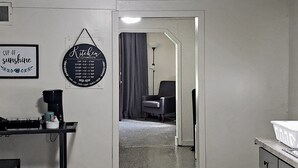 A kitchen with a coffee maker, a sign indicating coffee conversions, and a door leading to a living area.