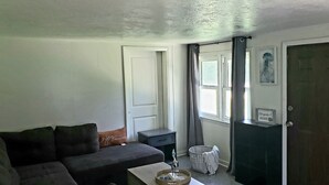 A living room with a dark-colored sofa, a small table with a tray, a basket, and a door with a sign.
